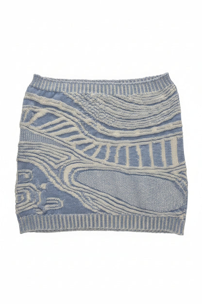 A light blue and off-white patterned knit sweater or cardigan laid flat on a beige carpet background.